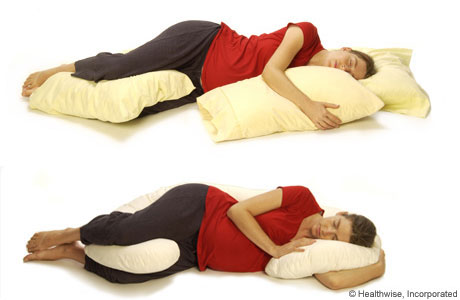Una mujer embarazada recostada de lado y apoyándose sobre almohadas