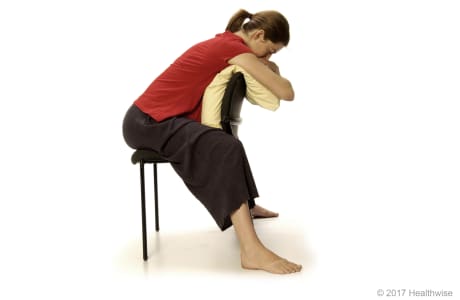 Person sitting backward in a chair and leaning forward over a pillow.
