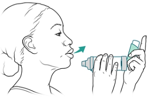 Person exhaling while holding inhaler and spacer near mouth.