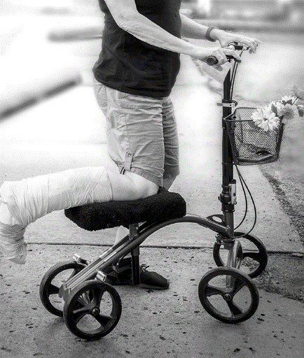 A person with a cast on their leg using a knee scooter outside on a paved surface.