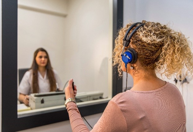 woman with headphones looking at audiologist through window